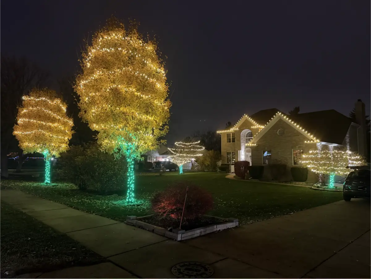Wrapped trees and roofline lighting on a two-story brick home