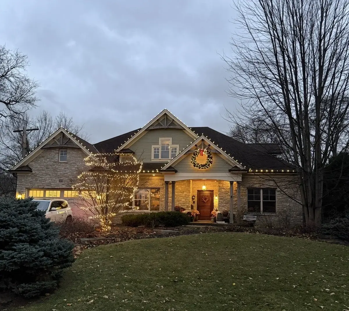 Craftsman home at dusk with roofline lights, wreath, and lit tree